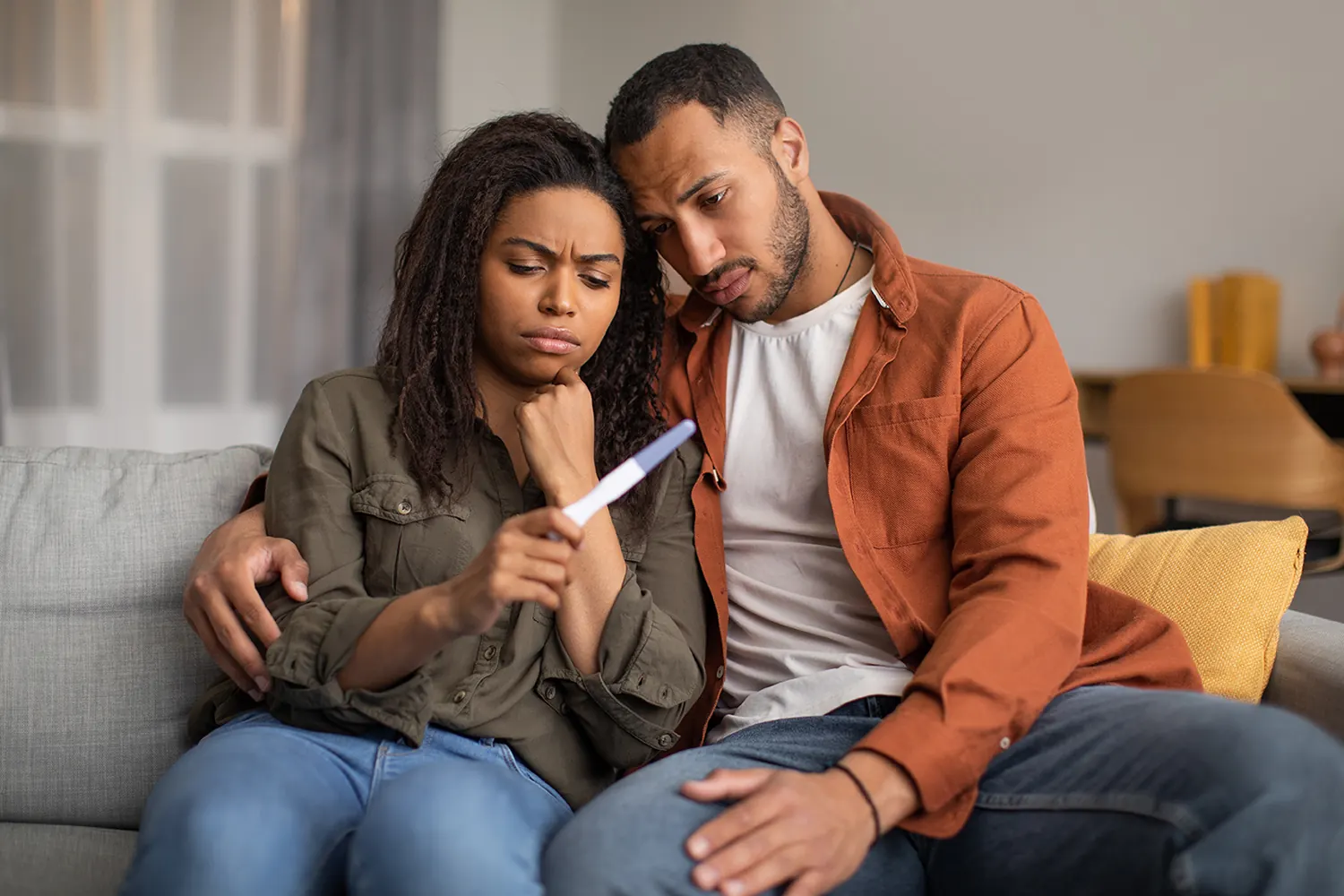 Infertility Problem. Depressed Black Couple Holding Negative Pregnancy Test Hugging Sitting On Couch At Home. Reproduction Health Problem, Childbirth Issues Concept